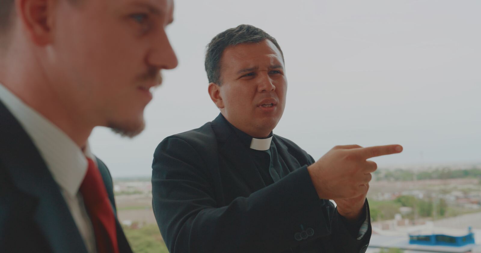 Father Cesar pointing out across the city, with Louis beside him